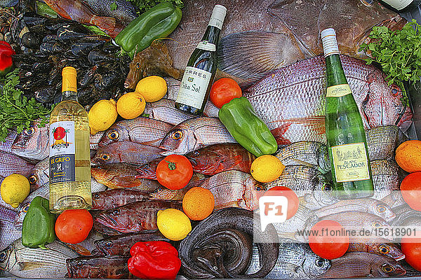 High Angle View Of Platter Of Locally Caught Fresh Fish With Wine Bottles And Raw Vegetables