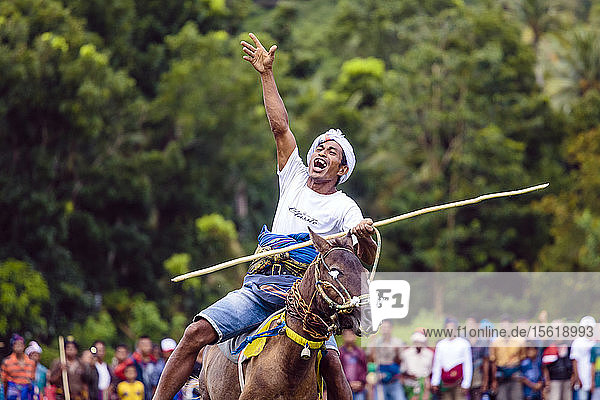 Mann hebt die Hand und reitet auf einem Pferd mit Speer beim Pasola-Fest  Insel Sumba  Indonesien