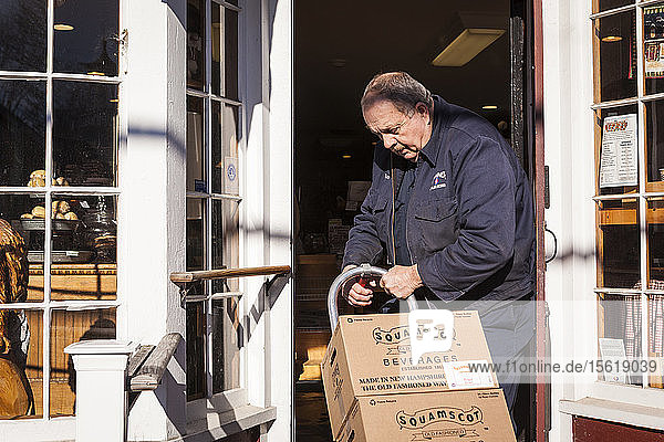 A man delivers cases of Squamscot soda to a general store.