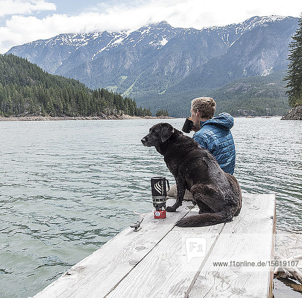 A man and his dog sit on a dock on Ross Lake in North Cascades National Park.