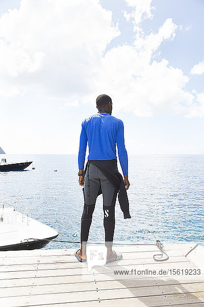 Scuba diver stands on dock looking out to horizon