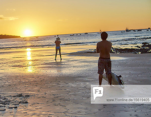 Ein Surfer sieht zu  wie eine Frau einen Sonnenuntergang in Costa Rica fotografiert