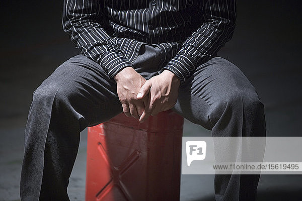 Cropped low angle front view of a young man sitting on a red 5 gallon gas can.