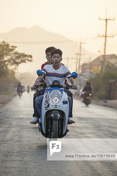Young men ride together on a motor scooter at sunset in Luang Prabang  Laos.