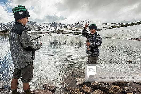 A boy grabs a trout caught by his twin brother  Matt  in order to unhook it  as the boys fish in Superior Lake  surrounded by large snow banks and reflecting snowy peaks  on the third day of Troop 693's six day backpack trip through the High Uintas Wilderness Area  Uintas Range  Utah