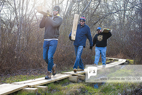 Freiwillige  die Bretter tragen  während sie gemeinsam einen Holzsteg als Teil eines Naturlehrpfads mit The Nature Conservancy bauen  Little Compton  Rhode Island  USA