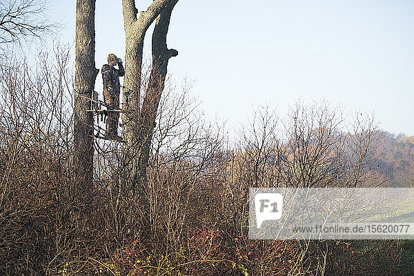 Junger erwachsener männlicher Jäger  der auf einem Baum steht und nach Rehen Ausschau hält