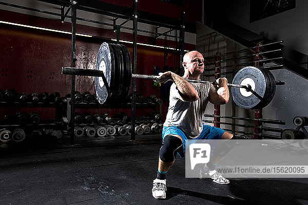 An athletic male works out with heavy weight on a barbell at gritty gym in San Diego  California.