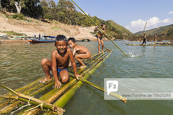 Kinder spielen im Nam Ou-Fluss auf Bambusflößen in Ban Hat Kham  Laos. Das Dorf würde durch den geplanten Staudamm Nr. 3 (mit dessen Bau noch nicht begonnen wurde) vollständig überflutet werden.