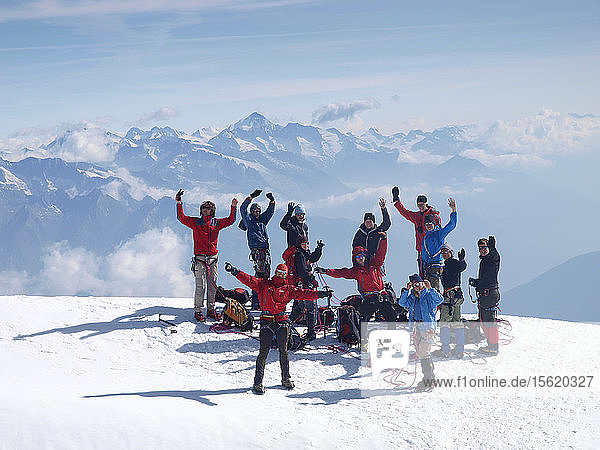 A group of young people are waiving while standing on a mountain top. They reached the summit of the Bishorn during a junior mountaineering course in the Swiss Alps.