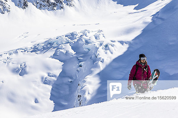 Professional Snowboarder Helen Schettini hikes to a ridge with a glacier in the background on a sunny day in Haines  Alaska.