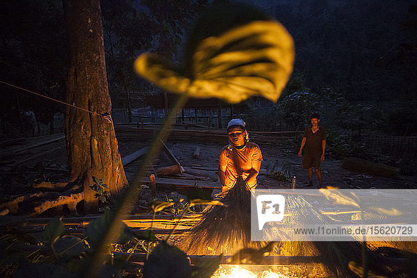 Eine Frau trocknet Schilfrohr über einem Feuer in Ban Pak Luang  Laos. Die mit Bambus umwickelten und zu Besen geformten Schilfrohrbüschel werden für 3.000 Kip (0 37 $) ins benachbarte Vietnam verkauft. Das Dorf würde durch den geplanten Staudamm Nr. 3 (mit dessen Bau noch nicht begonnen wurde) nur geringfügig überflutet werden.