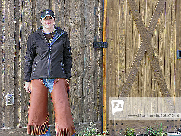 Vorderansicht einer lächelnden Frau in Chaps  die auf einen Ausritt auf einer Ranch wartet  Montana  USA