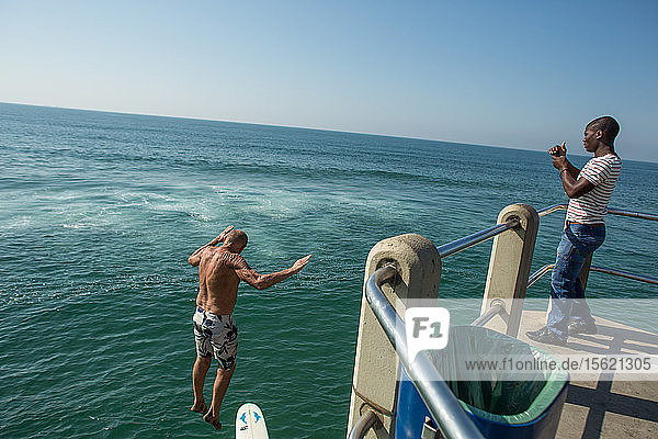 Mann beobachtet einen älteren Surfer  der mit seinem Surfbrett vom Pier an der Goldenen Meile springt  Durban  Südafrika