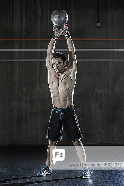 Ein männlicher Gewichtheber und CrossFit-Sportler ohne Hemd  der in einem CrossFit-Fitnessstudio einen Kesselglockenschwung ausführt.