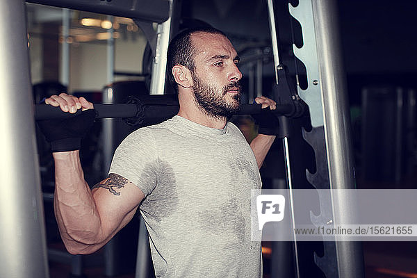 Portrait of muscular man training on special sport equipment in gym
