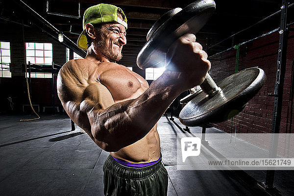 Ein Crossfit-Sportler führt Bizepscurls in einem alten  düsteren Fitnessstudio in San Diego  Kalifornien  aus.