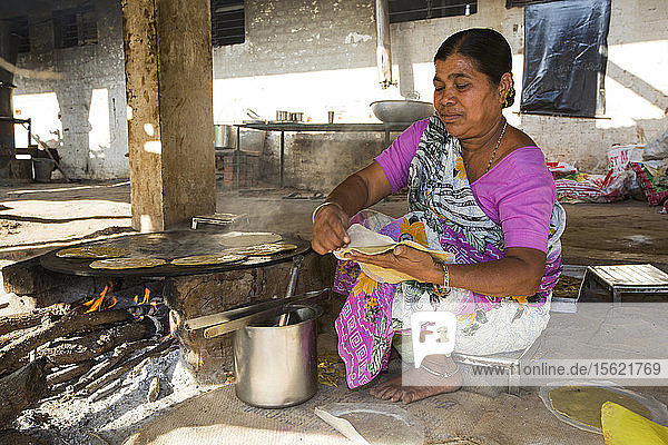 Der Muni Seva Ashram in Goraj  in der Nähe von Vadodara  Indien  ist eine ruhige Oase der humanitären Fürsorge. Der Ashram ist äußerst nachhaltig und wird nächstes Jahr völlig kohlenstoffneutral sein. Die ersten Sonnenkollektoren wurden 1984 installiert  lange bevor der Klimawandel auf der Tagesordnung stand. Die Energieversorgung erfolgt über Sonnenkollektoren und Holz  das auf dem Gelände angebaut wird. Lebensmittelabfälle und tierische Exkremente werden in Biogas umgewandelt  mit dem die Autos des Anwesens betrieben und auch zum Kochen verwendet werden. Außerdem werden Solarkocher verwendet  und die Klimaanlage des Krankenhauses wird mit Solarenergie betrieben. 70 % der verwendeten Lebensmittel werden auf dem Landgut angebaut. Es gibt ein Waisenhaus  Schulen für alle Altersgruppen  Berufsausbildung  Altenpflege  ein spezialisiertes Krebskrankenhaus mit hochmodernen Maschinen und sogar ein solarbetriebenes Krematorium. Diese Aufnahme zeigt einen Koch bei der Zubereitung von Chapatis auf einem Biobrennstoffofen.