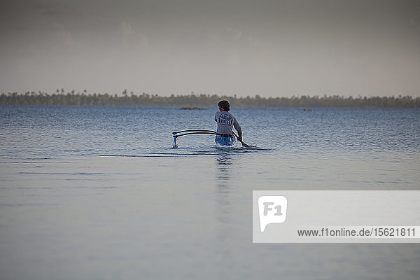 Foto mit Rückansicht eines jungen Mannes  der in einem Auslegerkanu bei Sonnenuntergang paddelt  Anaa  Französisch-Polynesien