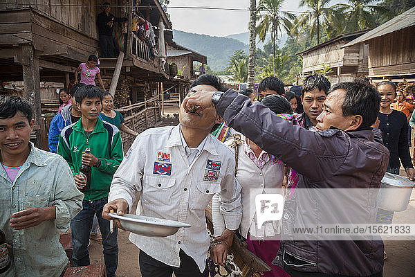 A man is offered a shot of lao-lao (rice whisky) at a wedding procession in Muang Hat Hin  Laos.