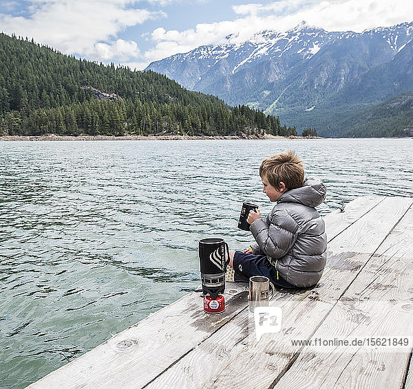 A boy sits on a dock drinking tea on Ross Lake in Washington's North Cascades National Park