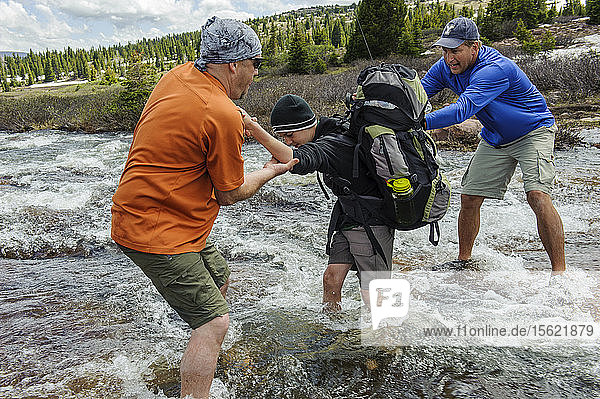 Zwei Männer helfen einem Jungen über einen reißenden Bach  einen Nebenfluss des Yellowstone Creek  in der alpinen Tundra unterhalb des Kings Peak  am vierten Tag der sechstägigen Rucksacktour von Troop 693 im High Uintas Wilderness Area  Uintas Range  Utah