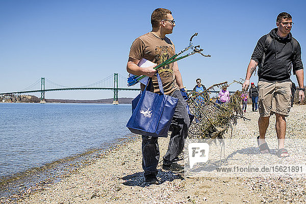 Zwei Männer tragen einen mechanischen Greifer  einen Müllsack und Müll bei der Strandsäuberung am Earth Day  Portsmouth  Rhode Island  USA