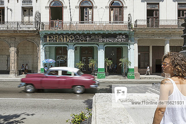 Touristisches Mädchen in den Straßen von La Habana mit einem alten Auto  das sich im Hintergrund bewegt
