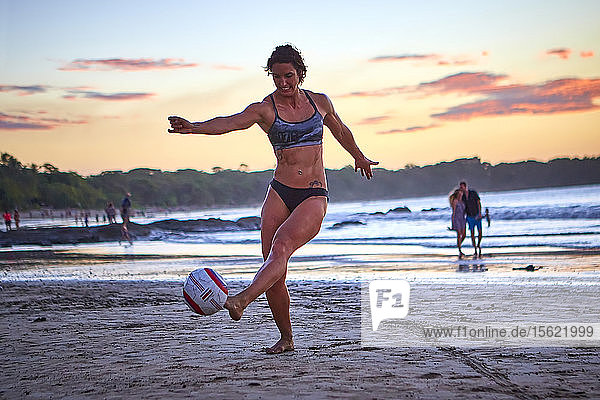 Fußballspieler übt bei Sonnenuntergang am Strand
