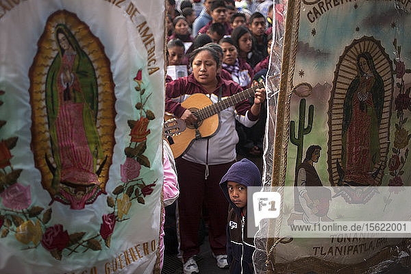 Ein Junge steht hinter einem Wimpel der Jungfrau von Guadalupe während der jährlichen Pilgerfahrt zur Basilika Unserer Lieben Frau von Guadalupe auf dem Tepeyac-Hügel in Mexiko-Stadt  Mexiko. Guadalupe ist bei den Eingeborenen als Tonantzin bekannt  was in der mexikanischen Sprache Nahuatl Unsere Mutter bedeutet. Jedes Jahr kommen Millionen von Menschen zu dieser Wallfahrt.
