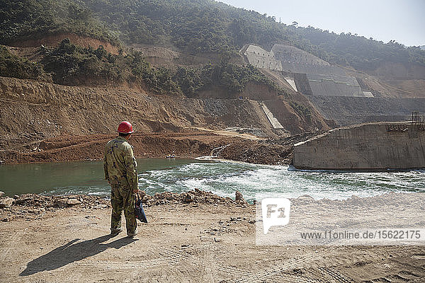 Ein chinesischer Arbeiter blickt über den Nam Ou Fluss in Laos auf die Baustelle des Staudamms Nr. 5. Unsere Packrafts (Mitte) vermitteln ein Gefühl für den Maßstab.