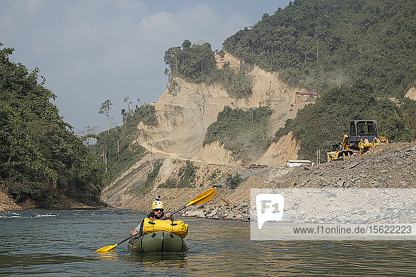 Robert Hahn paddelt mit seinem Packraft an der Baustelle des Staudamms Nr. 6 am Nam Ou Fluss in Laos vorbei. Die Zufahrtsstraße schlängelt sich in steilen Serpentinen am Hang oberhalb des Flusses entlang.