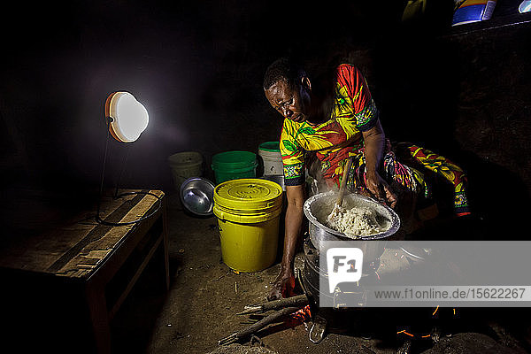 In ihrem Haus in der Nähe von Arusha  Tansania  bereitet die Solarunternehmerin Julieth Mollel ein Abendessen aus Ugali  Gemüse und Bohnen vor  das sie auf ihrem sauberen Kochherd zubereitet. Ugali ist ein Grundnahrungsmittel  das in vielen Ländern Afrikas gegessen wird  und besteht aus Maismehlbrei. Die nächtliche Arbeit in ihrer kompakten Außenküche wird durch den sauberen Herd erleichtert  der sehr wenig Rauch entwickelt und nur einen Bruchteil des Brennholzes eines traditionellen Drei-Steine-Kochers verbraucht  und durch die Solarlaterne von Solar Sister  die den Raum während der Arbeit hell erleuchtet. Julieth Mollel hat kein einfaches Leben gehabt. Julieth und ihr Mann gehören dem Stamm der Massai an und leben im Norden Tansanias  etwa eine Stunde außerhalb von Arusha  an den Südhängen des Mount Meru. Julieth hat ihr ganzes Leben lang in der Landwirtschaft geschuftet  Ernten verkauft und den Haushalt für ihren Mann und ihre Kinder geführt. Jetzt  mit einundsechzig (61) Jahren  arbeitet sie hart  um die Familie zu ernähren und die Schulgebühren für ihre Enkelkinder zu bezahlen. Bis sie begann  für Solar Sister in Tansania zu arbeiten  war das Leben für Julieth fast unerträglich geworden. Beim Kochen auf ihrem traditionellen Herd  der aus drei Steinen und einer offenen Feuerstelle bestand  entstand viel Rauch  den sie einatmete  wenn sie das Frühstück  Mittag- und Abendessen für ihre Familie kochte. Der Herd benötigte viel Brennholz  so dass sie täglich hinausgehen und ein großes Bündel Holz nach Hause bringen musste. Mit der Zeit bekam sie starke Schmerzen in der Brust und hatte Schwierigkeiten  das Brennholz aufzulesen und nach Hause zu tragen. Im Laufe der Jahre musste Julieth immer weiter laufen  um Brennholz zu bekommen  weil in der Gegend Bäume gefällt wurden  um Farmen zu vergrößern und Siedlungen zu bauen  und weil Brennholz zum Kochen und zur Herstellung von Holzkohle gesammelt wurde. In dieser Zeit kämpfte Julieth darum  das Schulgeld für ihre Enkelkinder zu bezahlen  aber es wurde immer schwieriger und sie war fast am Ende ihrer Kräfte und verzweifelt. Sie wusste?????? nicht  wie sie das schaffen sollte.