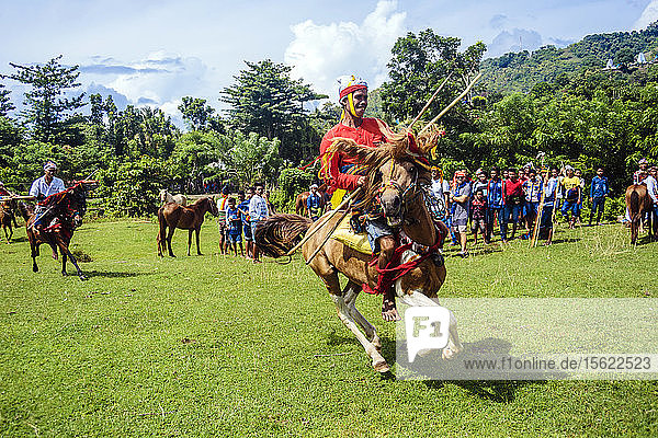 Junger Mann in Tracht reitet auf einem Pferd und hält einen Speer beim Pasola-Festival  Insel Sumba  Indonesien