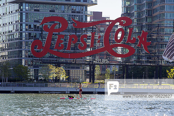Adult womanï¾ paddle boardingï¾ on East River with large soda company logo in background New York City New York USA