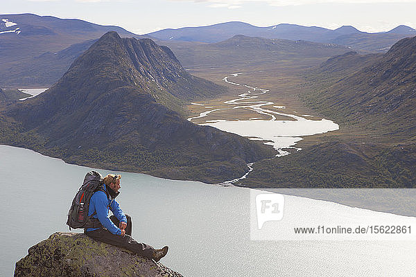 Ein Wanderer genießt die Aussicht auf Fjorde und Berge  während er auf einem Felsen des berühmten Besseggen-Kamms in Norwegen sitzt. Diese eintägige Überquerung im Jotunheimen-Nationalpark ist die beliebteste Wanderung in Norwegen.