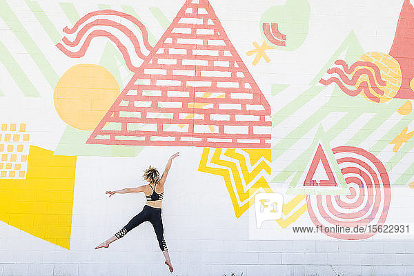 Junge  aktive Frau springt draußen vor eine Graffitiwand