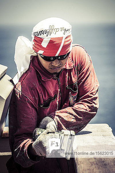 Seaman sanding a railing on a container ship while at sea.