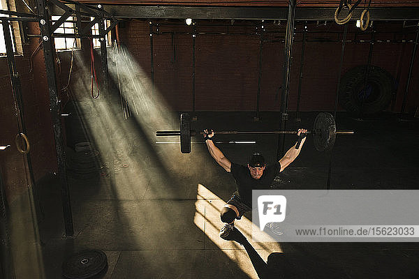 Eine Person  die Crossfit in einem alten Lagerhaus-Fitnessstudio macht  in dem Lichtstrahlen durch die Fenster eindringen.