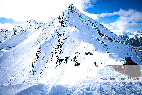 Ein Snowboarder sitzt auf einer Felsnase  bevor er den Silverton Mountain in Colorado hinunterfährt.