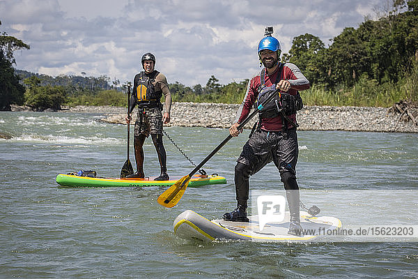 Photograph of two men posing for picture while paddleboarding on stand-up paddleboards  Peruvian Amazon  Manu National Park  Peru