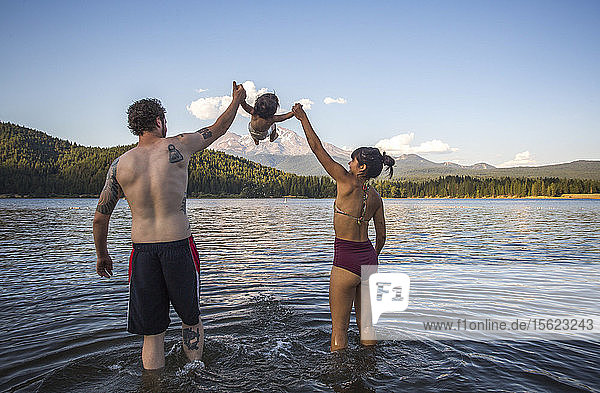 Rear view of couple in swimsuits playing with baby daughter in Lake Siskiyou  California  USA