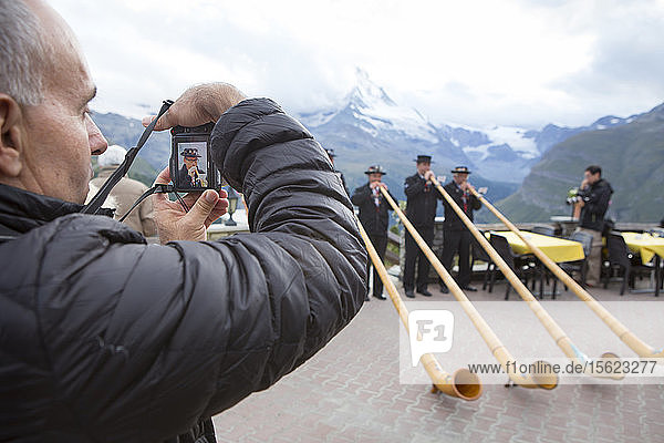 A tourist is taking a picture of four traditionally dressed locals of Zermatt play the Alphorn in front of the Matterhorn mountain. With the passing of time  the alphorn almost totally disappeared as an instrument used by Swiss shepherds. It was only with the romanticism of the 19th century and the revival of folklore and tourism that the alphorn experienced a renaissance and even became a national symbol.
