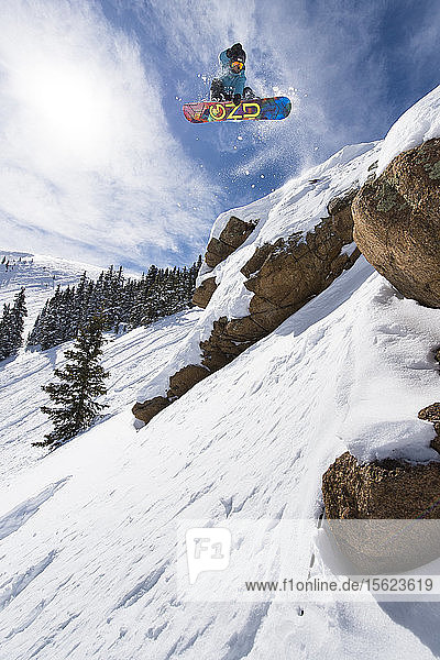Female Snowboarder Jumping On Rock In Colorado