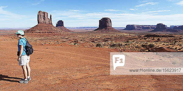 Eine Wanderin steht allein im Monument Valley und den Sandsteinfelsen.