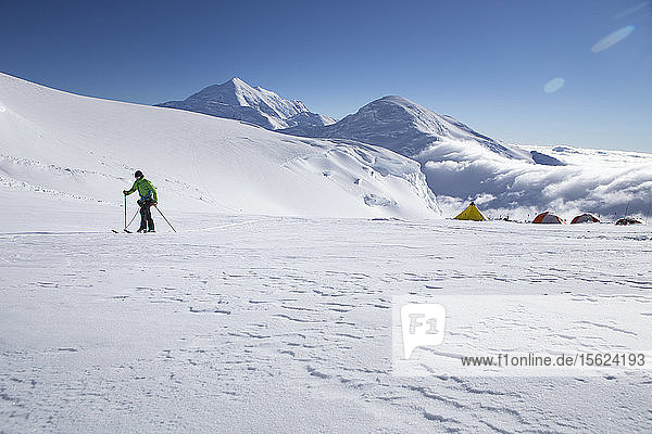 A ski mountaineer on the Kahiltna glacier of Denali National Park in Alaska  with mount Foraker and Kahiltna Dome in the background. On the right are the tents of 11 K Camp on Denali visible.