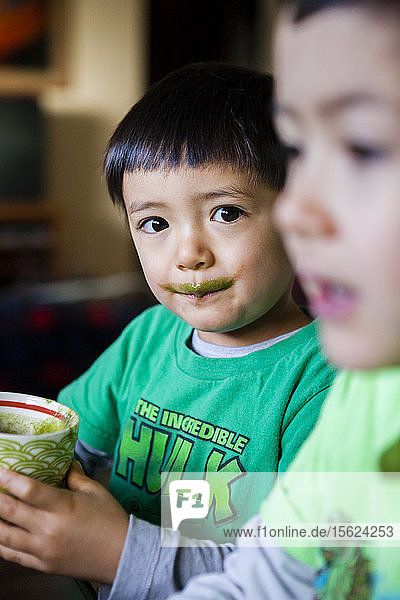 Ein 4 Jahre alter japanisch-amerikanischer Junge trinkt seinen morgendlichen grünen Smoothie neben seinem 6-jährigen Bruder.
