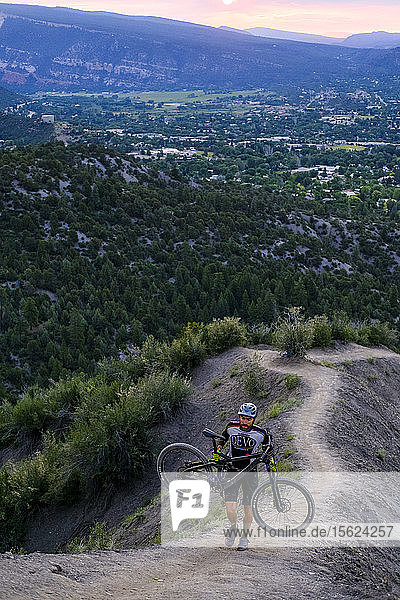 Male Mountain Biker in scenic landscape carries bike up Hogs back near Durango  Colorado  USA