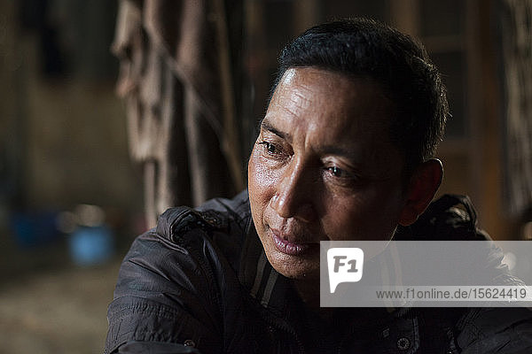 A man is lost in thought at his home while being asked questions about Nam Ou River Dam #6 which will inundate his village Ban Kor Man Mai Laos. He expressed sadness over the flooding of the riverside funeral sites but - having had two children die due to lack of medical care - appreciated the value of the road and other services promised at his future government provided home.