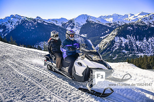 Man and woman riding snowmobile with mountain in background in Callaghan Valley  Whistler  British Columbia  Canada